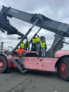 Étudiants en formation transport posant sur un engin de manutention reach steaker Fenwick lors d’une visite logistique professionnelle