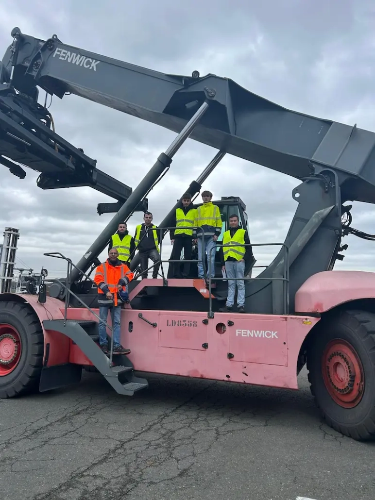 Étudiants en formation transport posant sur un engin de manutention reach steaker Fenwick lors d’une visite logistique professionnelle